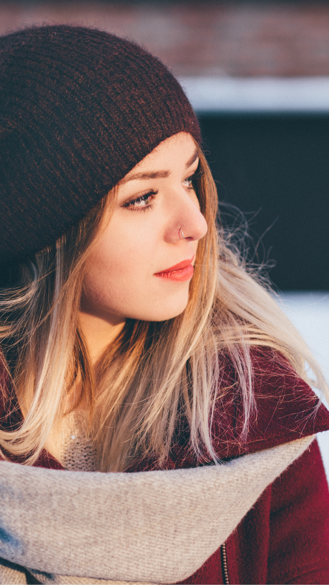 Portrait d'une jeune femme blonde en bonnet noir, regardant loin, hiver, écharpe beige et manteau rouge. barrière cutanée définition intégrée naturellement.