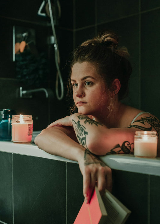 A woman relaxes in a bath, candles lit around her. The image suggests a peaceful setting for introspection, relevant to understanding how emotional well-being affects skin health (related to the article).
