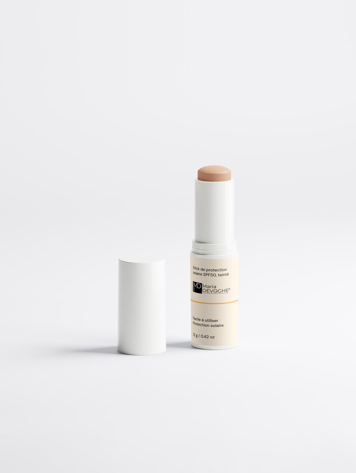 Stick de protection solaire SPF50, teinté, avec son capuchon posé à côté sur fond blanc.