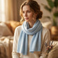 Echarpe en pur cachemire Sophia drapée autour du cou d’une femme, couleur bleu clair, intérieur chaleureux.