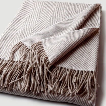 Plaid en cachemire Anatole plié sur fond clair, motif rayé beige et crème avec franges détaillées.