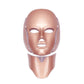 Masque LED pour visage et cou, couleur rose doré, vue frontale montrant les ouvertures pour les yeux et la bouche avec sangles latérales.