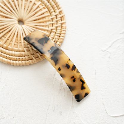 Barrette tortoise en résine marron clair et noir, longueur 9 cm, posée sur un dessous rond en rattan.