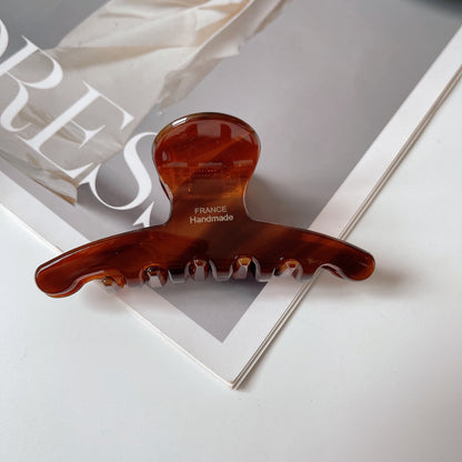 Peigne à cheveux artisanal en résine brun translucent, marqué "FRANCE Handmade" sur le dessus, posé sur un magazine.