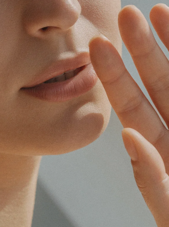 Lèvre et bouche d’une personne proche, avec les doigts près du visage, suggérant une routine de soin pour peaux sensibles, associée au Nettoyant à base d'huile et de lait pour peaux sensibles.