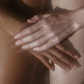 Crème pour le corps 5% Urée + 2% Panthenol: deux mains se caressant mutuellement, peau claire et peau foncée en arrière-plan.