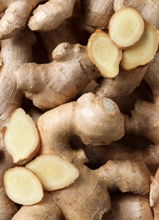 Gros plan sur du gingembre frais tranché, morceaux beige clair et peau rugueuse.