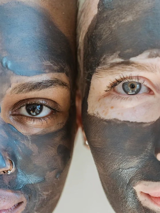 Deux visages encadrés, masqués de pâte d’argile bleu et noire couvrant la peau, yeux visibles au centre.