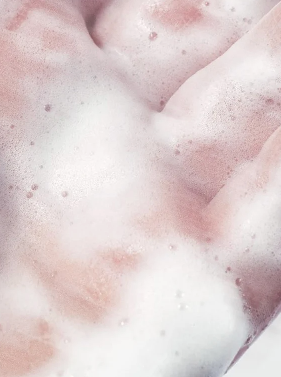 Pâtes mousseuses roses sur peau lavée, aspect clair et aérien, démontrant le nettoyant visage purifiant anti-acné en action.