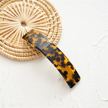 Barrette style tortoise avec motif marron et noir, pièce incurvée de 9 cm posée sur un dessous en rotin.